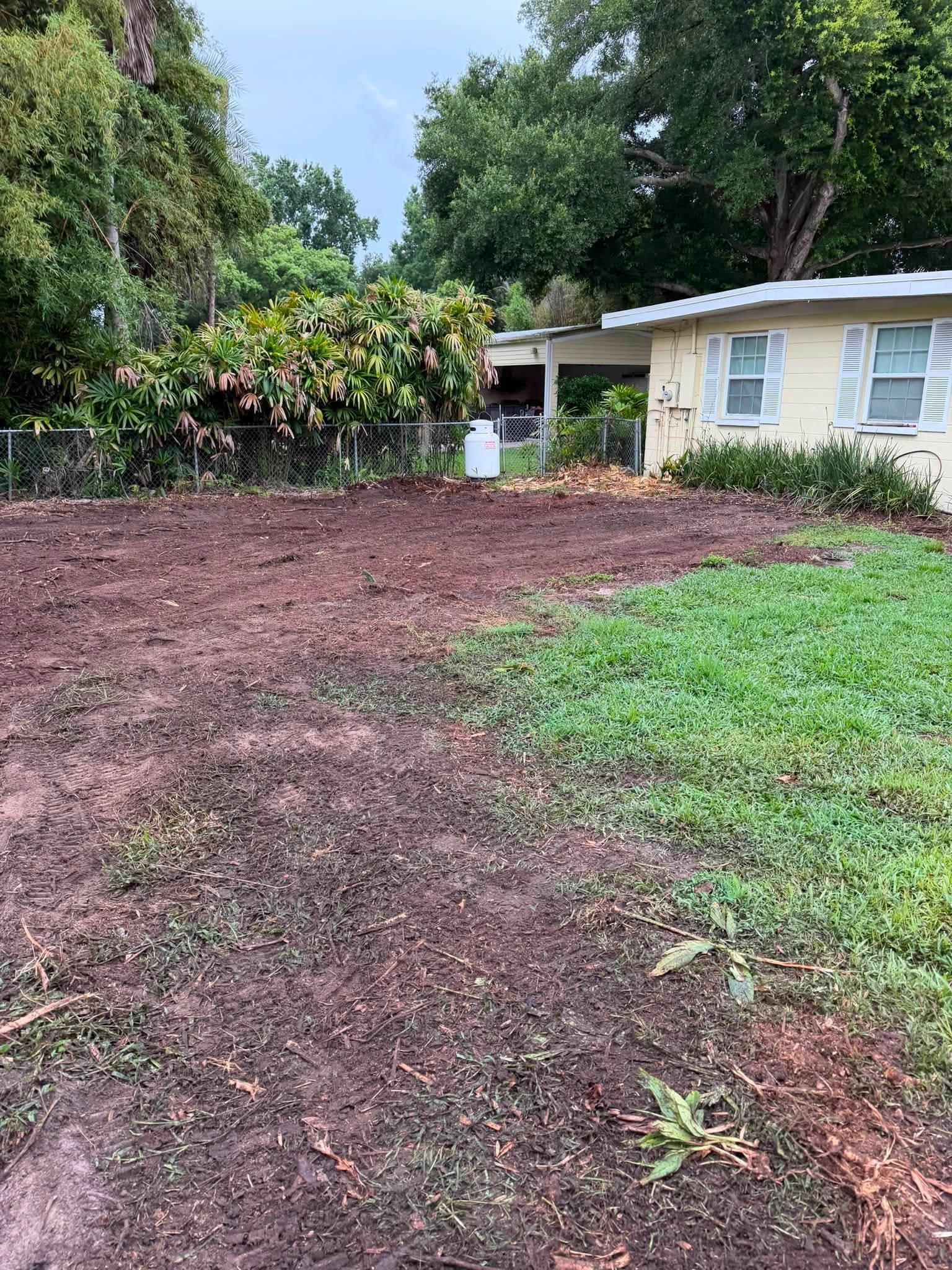 Cleared ground beside a home with surrounding lawn and trees.