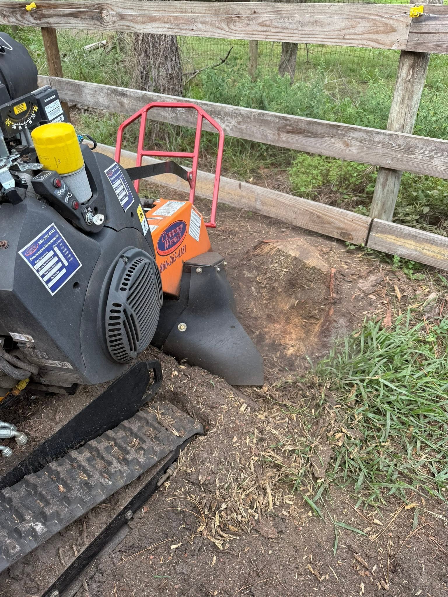 Stump grinder working beside a wooden fence.