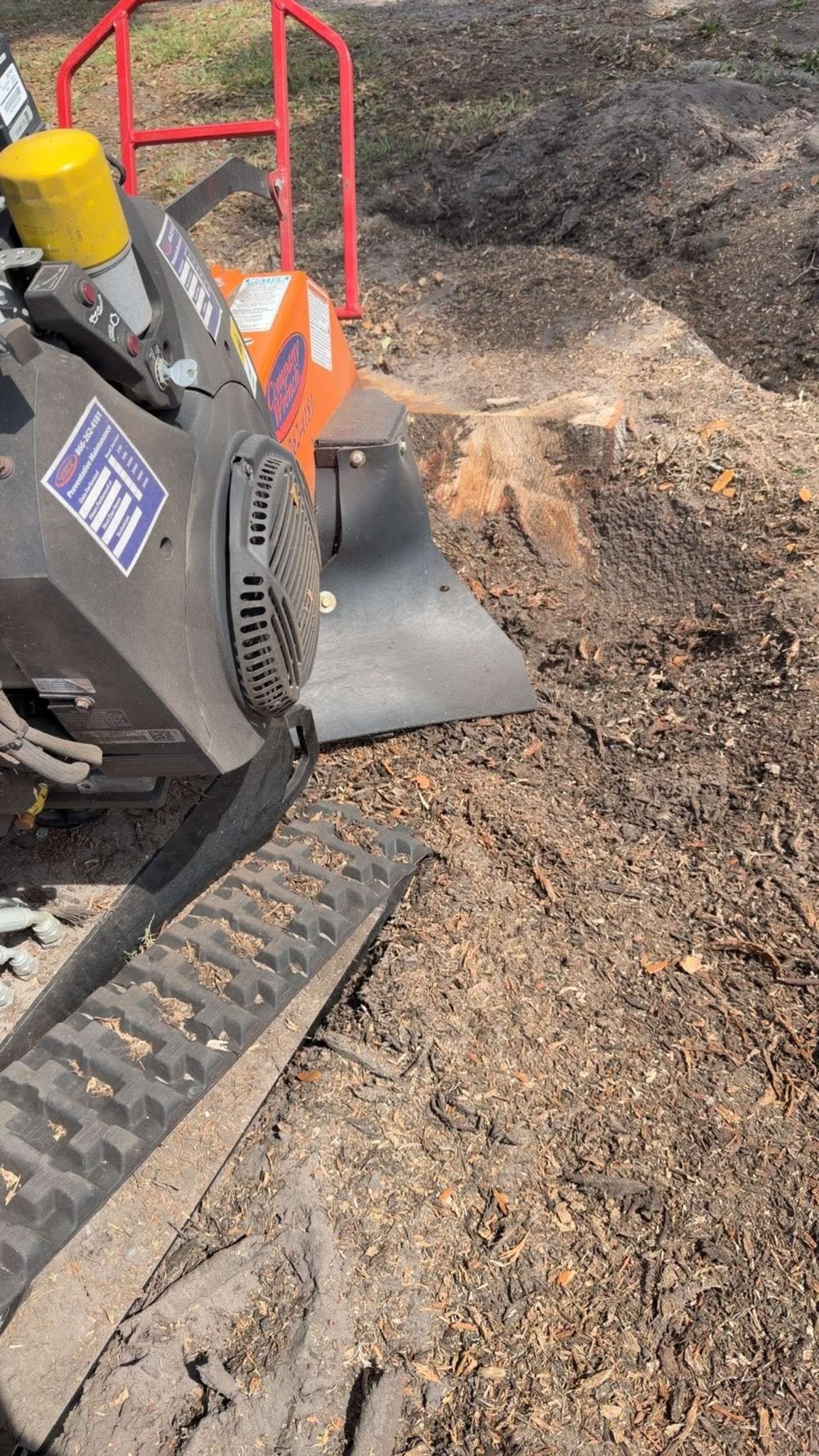 Stump grinder beside a partially ground stump surrounded by wood chips.