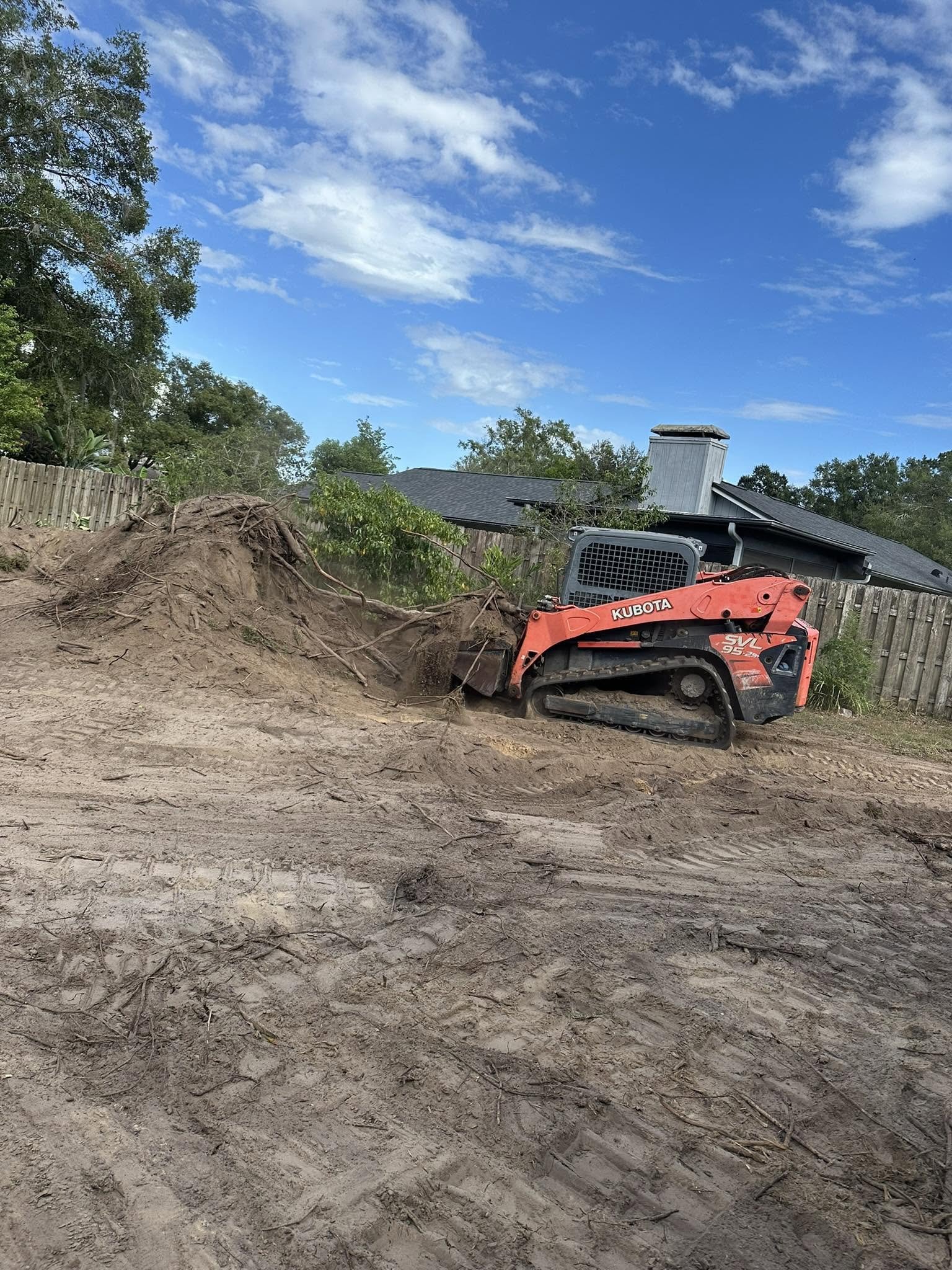 Compact track loader moving soil and roots on a residential property.