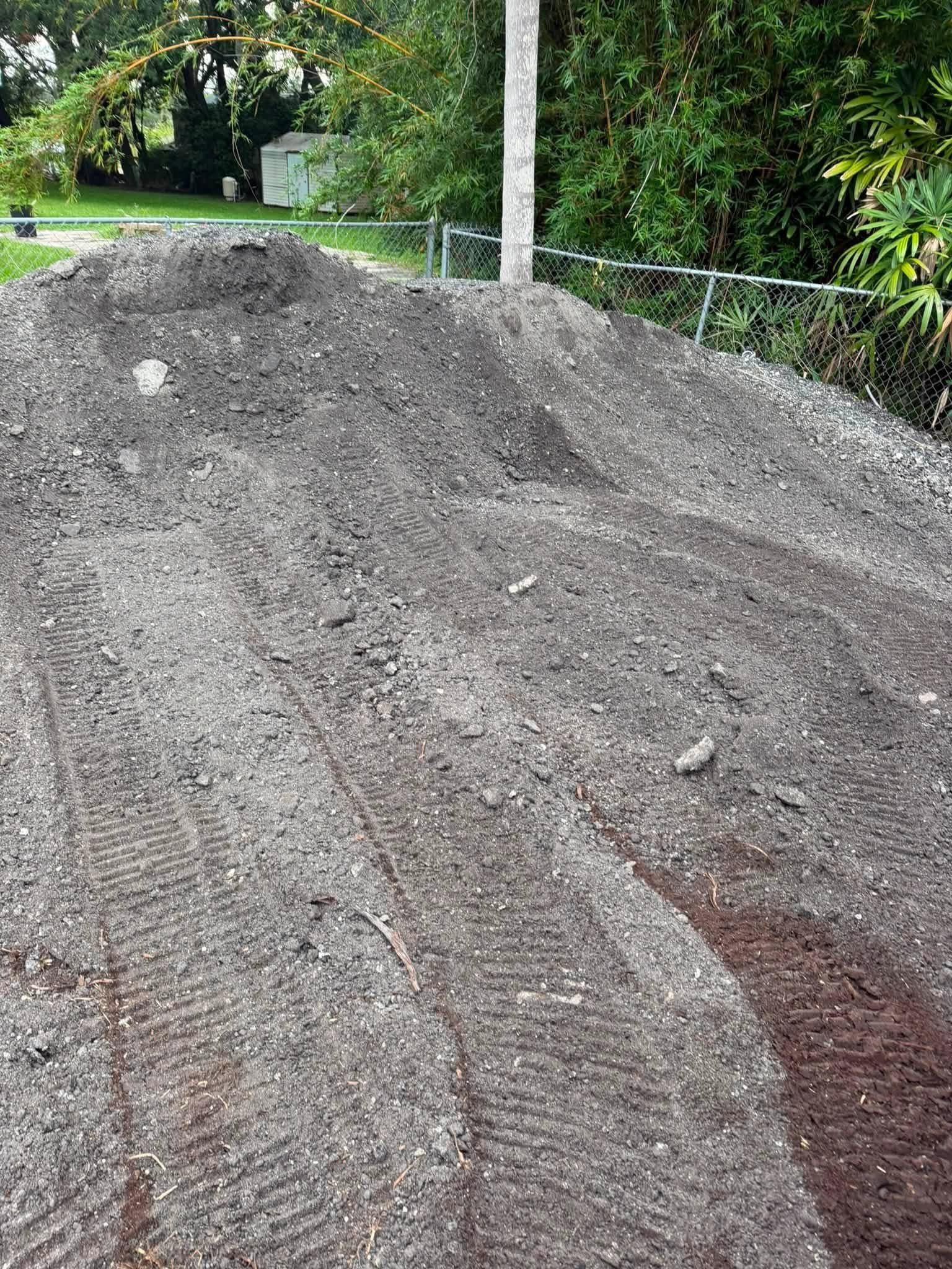 Piles of asphalt and equipment tracks in a fenced residential yard.